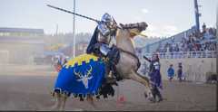 A jousting knight in blue and gold caparison riding at a Renaissance faire arena